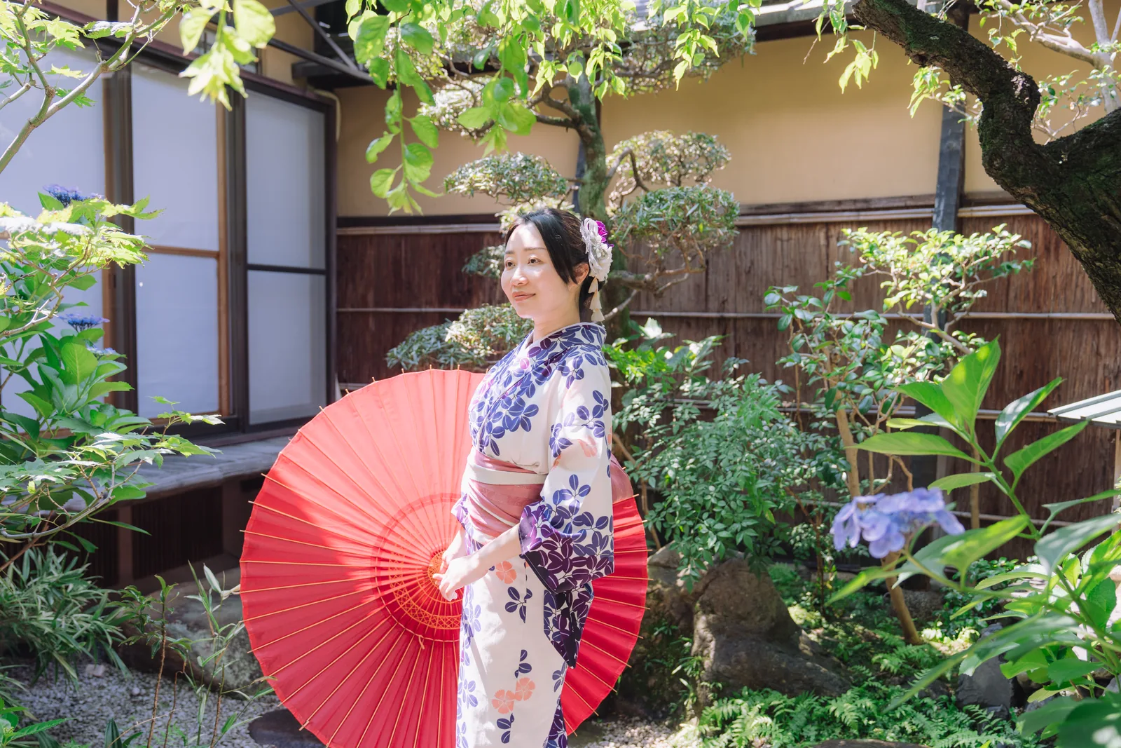 A guest in kimono with a red parasol in the garden